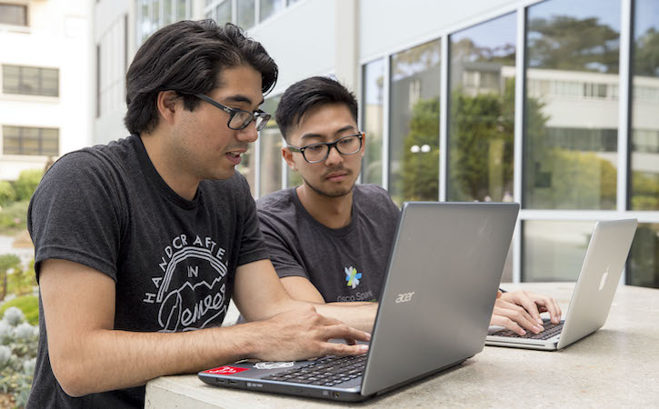 Two students sitting outside at a table with their laptops