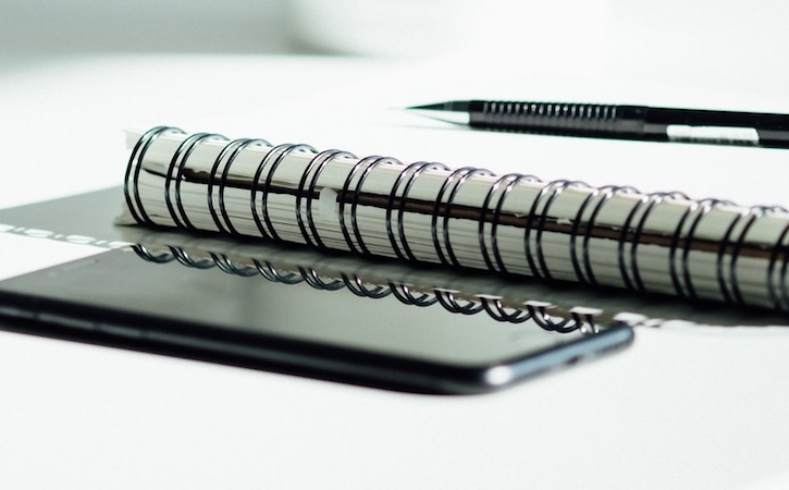 Spiral notebook, pen and phone on a table